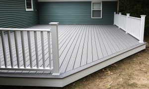 A gray composite deck with white railing attached to a home with blue siding.