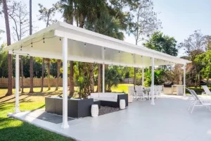 A white, freestanding patio cover over a concrete patio with beautiful furniture.